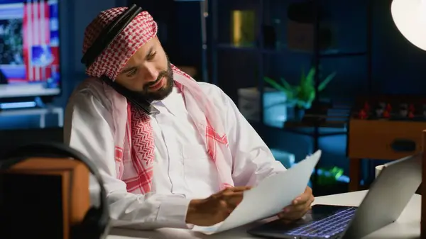 在舒适的办公室远程工作的同时 与同事进行电话交谈的阿拉伯员工 通过智能手机与同事交谈 讨论文书工作 — 图库照片