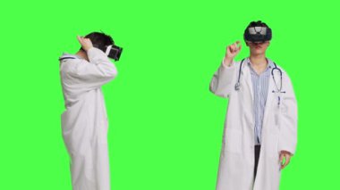 Hekim, sanal gerçeklik gözlüklü hastalara danışmanlık yapıyor, yeşil perde arkaplanına karşı beyaz önlük giyiyor. Pratisyen hekimler yapay zeka etkileşimli kulaklık kullanır. Kamera B.