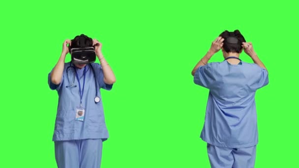 医療アシスタントは インタラクティブなVrメガネを使用して病気の治療をチェックし 仮想現実のヘッドセットとレンズを持つ患者の検査ファイルを調べます グリーンスクリーン背景の看護師 カメラ — ストック動画