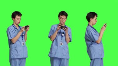 Akıllı telefon uygulamasında mobil video oyunu oynayan tıbbi asistan, sağlık hizmetlerine ara veriyor. Hemşire telefonda, yeşil ekran arkaplanının önünde duran bir oyun turnuvasından hoşlanıyor. Kamera B.