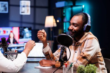 Gülümseyen siyah adam radyo yayınına başlamadan önce Afrikalı Amerikalı sunucuyla yumruk tokuşturuyor. Çevrimiçi talk show 'un kayıt sırasında, neşeli erkek etkeni misafiri selamlıyor.