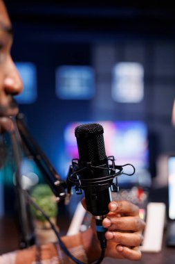 Erkek sunucu, evdeki profesyonel ses ekipmanlarını kullanarak canlı sohbet programı kaydediyor. Afrikalı Amerikalı bir adam mikrofona konuşuyor çevrimiçi bir prodüksiyon yapıyor, bir podcast bölümü yaratıyor.