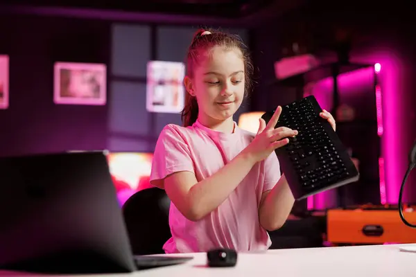 Stock image Happy charismatic girl presenting latest gaming computer peripheral tech on her internet channel in neon lit apartment. Trending influencer kid filming review of wireless Bluetooth mechanical keyboard