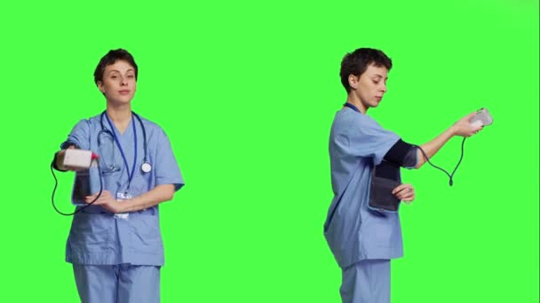 動脈血圧を測定するために使用されるテノメータを示す医療アシスタントは 緑色の背景に立っています スパイグマノメーターツールを使用して チェックイン時に測定を行う看護師 カメラ — ストック動画