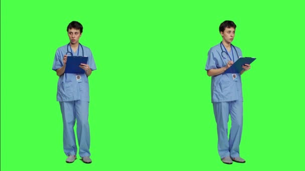 医疗助理在剪贴板文件上填写检查信息 做笔记 并用清单预约医生 穿着蓝色刷子的护士站在绿屏的背景下 相机A — 图库视频影像