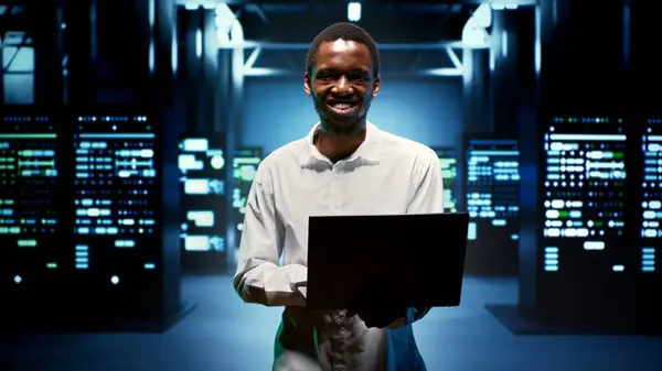 Computer scientist walking between data storage devices in computing server room, ensuring proper operations conditions. Serviceman monitoring high tech facility infrastructure energy consumption