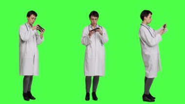 Pratisyen hekim cep telefonu uygulamasında video oyunu oynuyor, yeşil perde arkaplanına karşı online oyun yarışmasıyla eğleniyor. Neşeli doktor internet oyunuyla rahatlıyor. Kamera A.