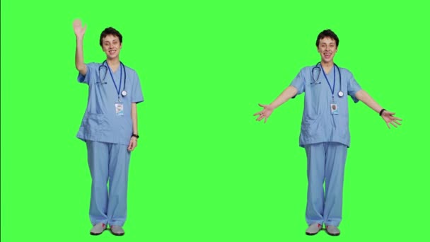 笑顔と振動で患者に挨拶する喜びの医療アシスタントは グリーンスクリーンの背景に対してスタジオで挨拶します 笑顔で元気な看護師が医療クリニックの人々を歓迎します カメラ — ストック動画