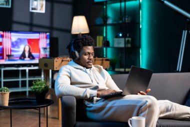 Afrikalı Amerikalı bir adam sıkılmış hissediyor, internette kayıyor müzik dinlerken dizüstü bilgisayar kullanıyor, hafta sonu dinleniyor. Kulaklık takan, internette sörf yapan biri.