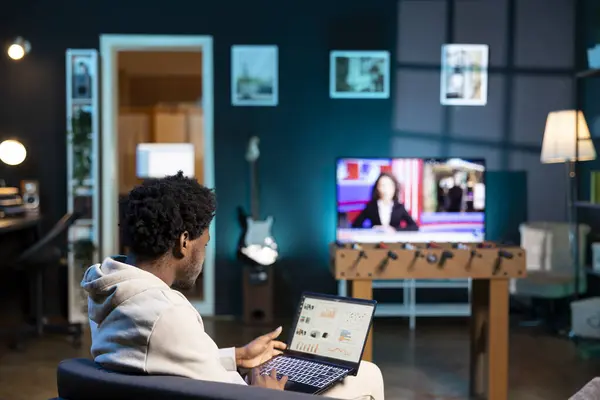 stock image Remote employee at home on couch looking at financial data on laptop screen. BIPOC man in apartment trying to complete job tasks before deadline, analyzing business charts