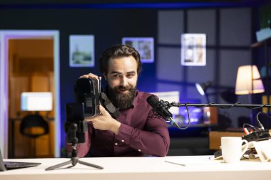 Seyircilere VR gözlüklerini sunan adam tripod dengeleyiciyle cep telefonuyla video çekiyor. Sanal gerçeklik ürünü değerlendiren içerik oluşturucu, profesyonel mikrofon ile kayıt