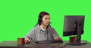 Genç oyuncu bilgisayar masasında oturuyor ve insanlarla web tabanlı video oyunları oynuyor, modern aletleri kullanarak iyi vakit geçiriyor. Asyalı kişi yeşil ekran için RPG yarışmasında yarışıyor.