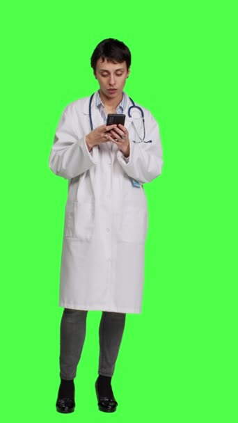 フロントビュー ソーシャルメディアアプリで人々をテキストにナビゲートする医師は 緑色の背景に立っています オンラインでウェブサイトを閲覧する白いコートの医学 チェックアップの予定を作る カメラ — ストック動画