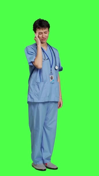サイドビュー グリーンスクリーン背景に頭痛を抱えているアンウェル看護師 スクラブを着用し 病院で過労を感じます 痛みを伴う片頭痛 ストレス バーンアウトを有する医療アシスタント — ストック動画