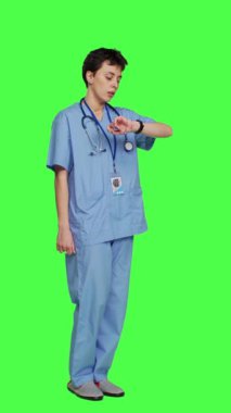 Nöbetteki stresli hemşire yeşil ekran arkaplanına karşı sabırsız davranarak hastanın sağlık kontrolüne gelmesini bekliyor. Ameliyat önlüğü ve steteskopu olan bir tıp asistanı.