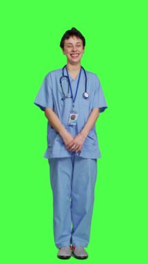 Neşeli gülümseyen tıp asistanı yeşil ekran arkaplanının karşısında duruyor, hastane önlüğü giyerken kendinden emin ve başarılı hissediyor. Hemşire cerrahı sağlık sektöründe çalışıyor.
