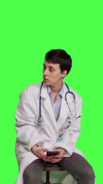 Stüdyoda akıllı telefon sosyal medya uygulamaları kullanan, yeşil ekran arka planına karşı bir sandalyede oturan kadın uzmanı. Doktor birini bekliyor ve internet sayfalarına bakıyor, mesajlaşıyor. Kamera B.