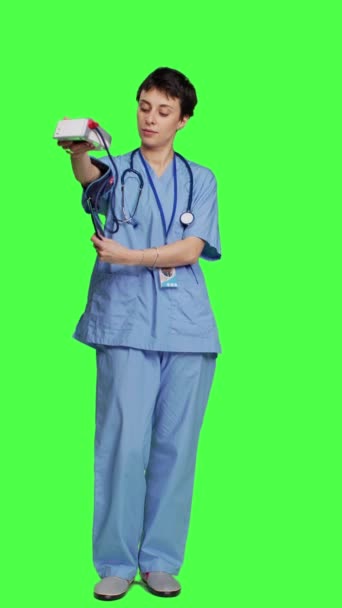 フロントビュー 動脈血圧を測定するために使用されるテノメーターを示す医療アシスタントは 緑色の背景に立っています Sphygmomanometerツールを使用してチェックイン時に測定を行う看護師 — ストック動画