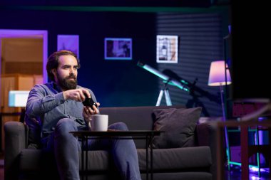 Sanal dünyaya dalmış, modern bir dairede kumanda elinde tutuyor, video oyunları oynuyor. Neşeli beyaz adam oturma odasının rahatlığıyla oyun oynamaktan zevk alıyor.