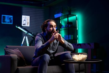 TV 'de dizi izleyen ve patlamış mısır yiyen bir adam, sürpriz bir şekilde ters köşe yapıyor, ekrana dikkatle bakıyor. Dairede koltukta oturan adam beklenmedik olaylar karşısında şok oldu.