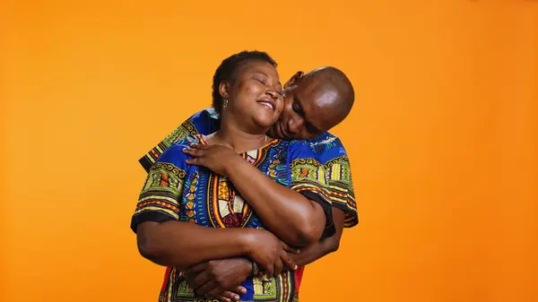 スウィート アフリカ系アメリカ人のカップルがスタジオで抱擁し お互いを抱き合い 誠実な気持ちを表現しています オレンジ色の背景に彼の妻を抱擁するエスニックロマンチックな男 — ストック写真