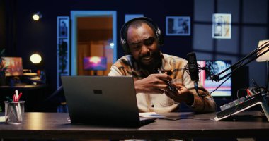 Afrika kökenli Amerikalı teknoloji uzmanının portresi RGB Işıkları 'nın oturma odası stüdyosunda yeni yayınlanan akıllı telefonu inceliyor. Profesyonel kamera kullanarak teknoloji kanalı vlog 'unu görüntüleyen etkili kişi