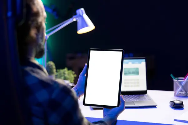 男人把平板电脑垂直地放在笔记本电脑前 屏幕上有一个孤立的白色屏幕 在家工作的男性自由职业者 专注于显示空白色键模拟模板的数字设备 — 图库照片