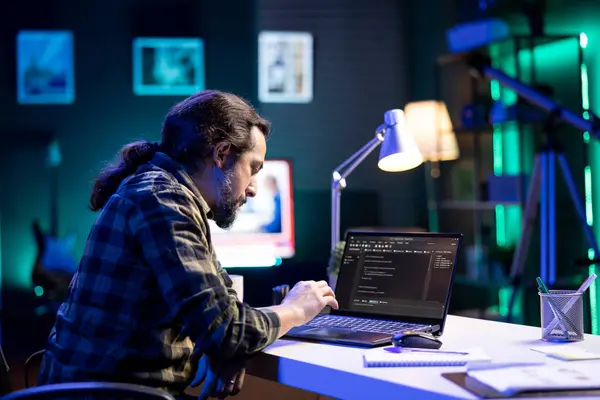 専用の男性プログラマーは 携帯コンピュータを使用してデータベースを管理し ネットワークセキュリティを監視します ひげ付き男はデスクに座っている間にデジタルラップトップでコーディングしています — ストック写真