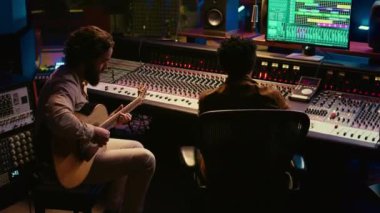 Yetenekli gitarist, elektro akustik gitar melodilerini ses düzenleme yazılımına kaydediyor ve ses mühendisiyle birlikte şarkısını hazırlıyor. Prodüksiyon sonrası kontrol odası. Kamera B.