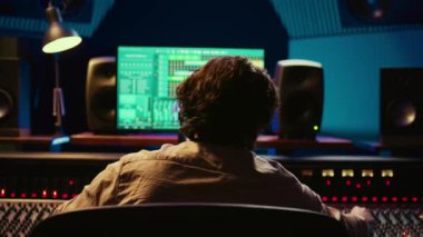 Müzik mühendisi, konsol ve daw yazılım arayüzünü karıştırarak yeni bir albüm üzerinde çalışıyor. Teknisyen hareket eden fadorlar ve renkli sayaçlar için ses konsolu kullanıyor. Kamera B.