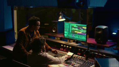 Müzisyen ve yapımcı profesyonel stüdyo istasyonunda ses yastıkları üzerinde çalışıyor. Ses tasarımcısı müzik yapımında dijital karıştırıcı kullanır, kaydırma çubukları ve kontrol masasındaki tuşlarla çalışır. Kamera B.