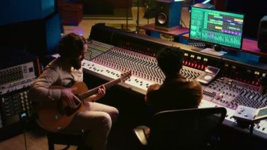 Profesyonel stüdyoda rock yıldızı gitarıyla müzik kaydediyor, kontrol odasında albümü için yeni bir müzik yaratıyor. Elektro akustik gitarda şarkı üreten sanatçı bestecisi. Kamera B.