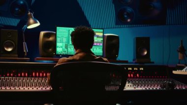 Afrika kökenli Amerikalı müzik yapımcısı profesyonel stüdyodaki yeni şarkısında kontrol odasında müzik karıştırıyor ve ustalaştırıyor. Teknisyen ses panelindeki düğmelere ve sürgülere basıyor. Kamera B.