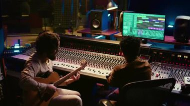 Yeni şarkılar kaydetmek için elektro akustik gitarıyla şarkı söyleyen yaratıcı sanatçı, profesyonel stüdyoda kontrol odasında müzik üretiyor. Yetenekli müzisyen bir albüm için yeni şarkılar yaratıyor. Kamera B.