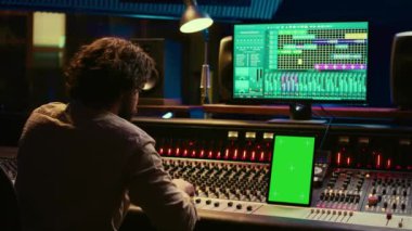 Profesyonel ses uzmanı, müzik stüdyosunda şarkıları karıştırıp ustalaştırıyor kontrol odasında düğmelere ve anahtarlara basıyor. Ses mühendisi melodileri yeşil ekran tabletle kaydediyor. Kamera B.