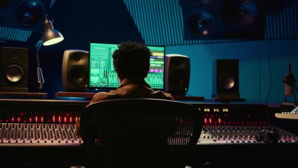 非裔美国人音乐制作人在他的专业工作室的新曲目中探索 在控制室中混音和掌握曲调 技术员按下声卡面板上的按钮和滑块 摄像头B — 图库视频影像
