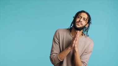 Pious Middle Eastern man praying to his god, asking for forgiveness, feeling desperate. Spiritual BIPOC man doing worship hand gesturing, confessing, begging for pardon, studio background, camera A clipart
