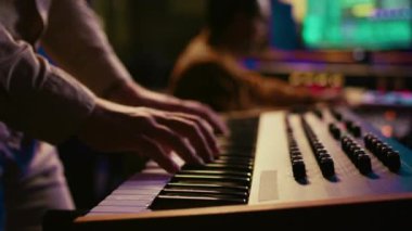 Müzisyen besteci profesyonel stüdyoda Midi kontrolör sentezleyicisi çalıyor, karıştırma konsolu üzerine müzik besteliyor. Kontrol odasında piyanonun elektronik klavyesinde performans sergileyen sanatçı. Kamera B.