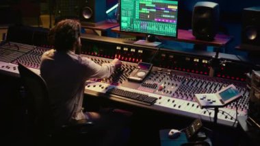 Müzik yapımcısı, tonsal dengesizlikleri veya beyaz gürültüyü, kontrol odasını yok etmek için konsol ve şalterleri karıştırarak sesleri düzenliyor. Teknisyen düğmeleri çeviriyor, ses seviyelerini ayarlıyor. Kamera B.