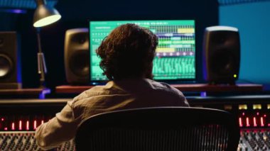 Müzik yapımcısı, kontrol odasında ses yazılımı ve karıştırma konsolu ile bir parça bitiriyor, sesleri işlemek için profesyonel stüdyoda teknik ekipmanlarla çalışıyor. Ses teknisyeni iş başında. Kamera A.