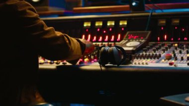 Afrika kökenli Amerikalı müzik yapımcısı, şarkıları kaydetmek ve montajlamak için düğmeler ve kaydırma çubuklarıyla karıştırma konsolu kullanıyor. Teknik teçhizatlı ses uzmanı sesleri. Kamera A.