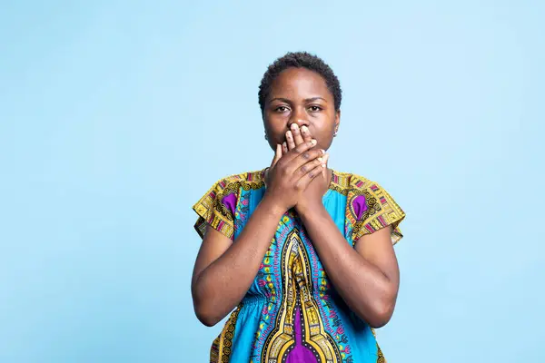 African american model covering her mouth to be silent, recreating three wise monkeys symbol to keep quiet in front of the camera. Woman showing inspirational traditional sign in studio.