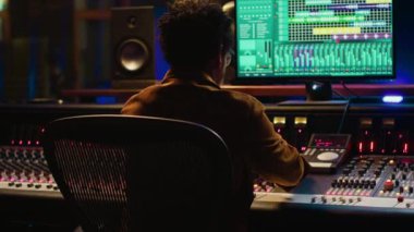 Ses tasarımcısı şarkıları karıştırıp ustalaştıktan sonra stüdyo sandalyesinde dinleniyor, kontrol odasında müzik projesini bitiriyor. Afrika kökenli Amerikalı ses uzmanı yeni şarkılar üretiyor. Kamera A.