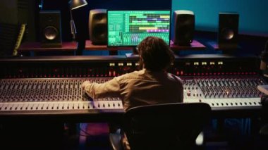 Müzik yapımcısı, kontrol odasında ses yazılımı ve karıştırma konsolu ile bir parça bitiriyor, sesleri işlemek için profesyonel stüdyoda teknik ekipmanlarla çalışıyor. Ses teknisyeni iş başında. Kamera B.