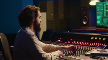 Kontrol odası ses mühendisi sürgülü ve düğmeli müzik düzenliyor, profesyonel ses geçirmez stüdyoda post prodüksiyon üzerinde çalışıyor. Müzik seti karıştırma konsolunda şarkı üreten teknisyen. Kamera A.
