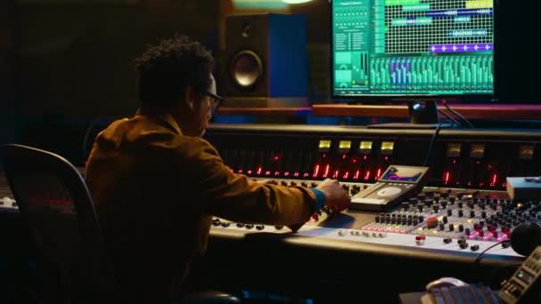 アフリカ系アメリカ人のオーディオ専門家は ポストプロダクションのトラックにサウンドエフェクトを追加し 混合コンソールを操作し スライダーをプッシュします プロデューサーは彼の新しいアルバム オーディオミキサーのための音楽を作成します カメラ — ストック動画