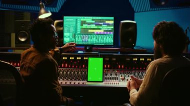 Yapımcı ve sanatçılardan oluşan bir ekip, profesyonel stüdyoda, kayıt seansından sonra şarkıları karıştırıp ustalaştıran bir tablet kullanır. Kontrol odasında konsolla çalışan uzmanlar. Kamera B.