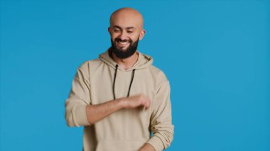 Orta Doğulu yetişkin stüdyoda dans figürleri sergiliyor. Mavi arka planda eğleniyor ve rahatlıyor. Stüdyoda dans eden ve kendinden emin hisseden genç adam, havalı adam. Kamera 1.