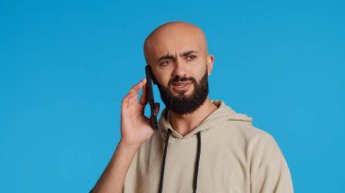 Orta Doğulu bir adam telefonla arkadaşlarıyla sohbet ediyor, mavi arka planda dikilirken akıllı telefonlara cevap veriyor. Modern adam uzak bir ağda bir şey tartışıyor. Kamera 2. El kamerasıyla..