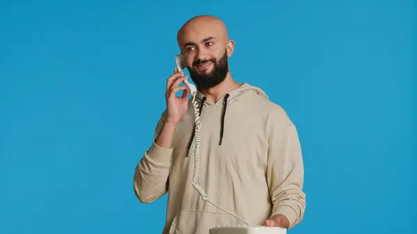 イスラム教徒の成人は コード付きのヴィンテージオフィス電話を使用して スタジオの地上電話に電話をかけます 青い背景の上に立って 遠隔電話について話し合うアラブの男 カメラ — ストック写真